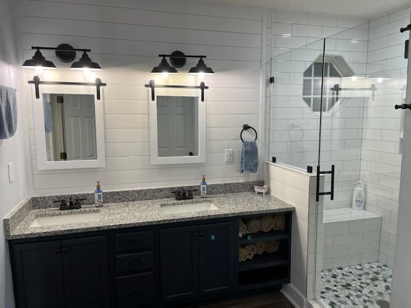 Double vanity with matte black sconces and a glass shower