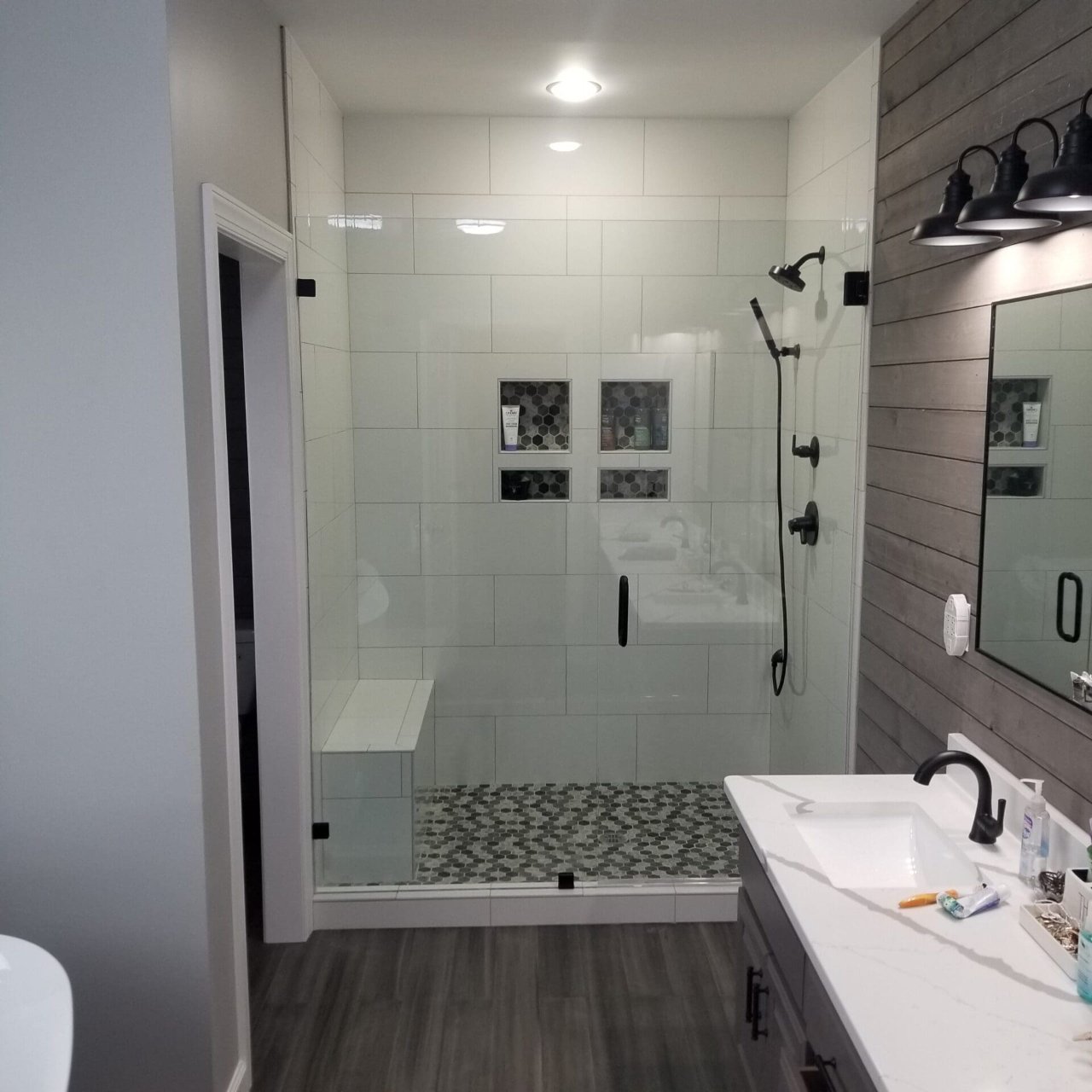 Walk-in shower with matte black fixtures and hex tile floor
