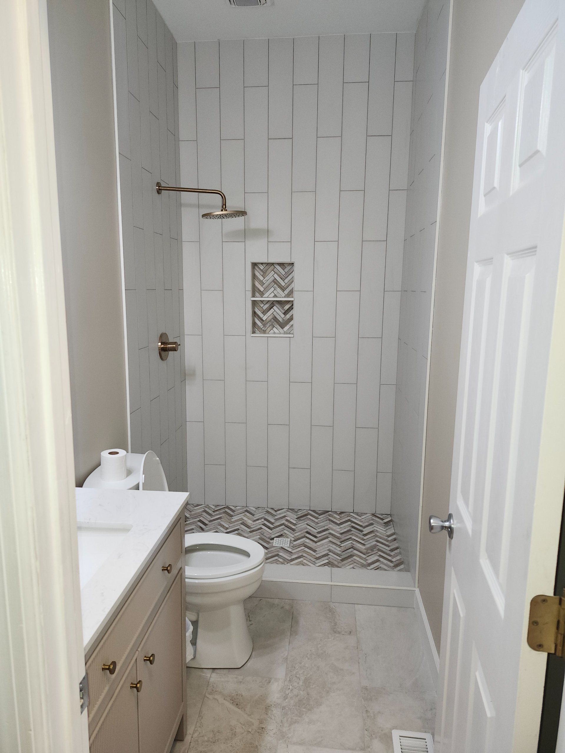 Tile shower with brass rain head and herringbone floor