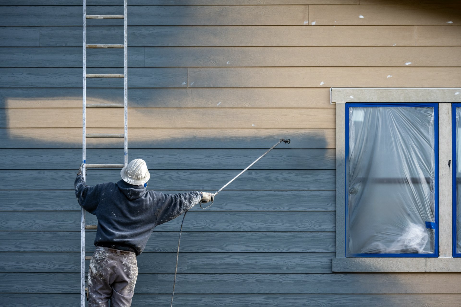 Painter spraying siding on a home exterior